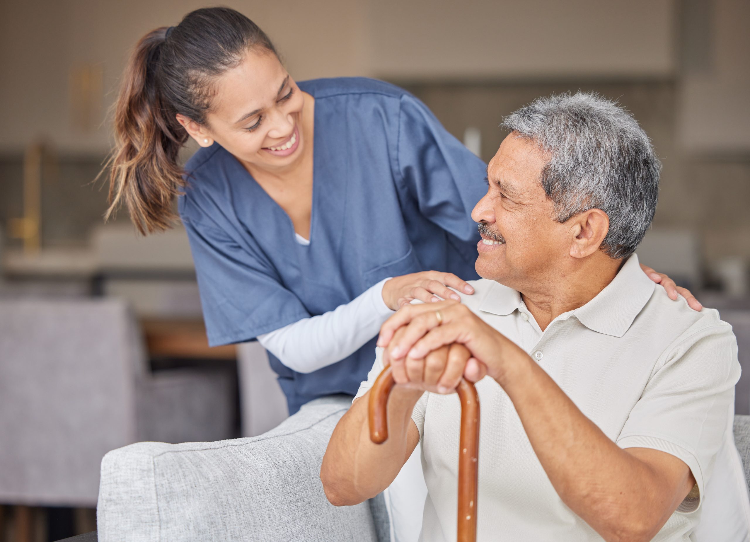 nurse helping elderly patient in assisted living Happy senior man bonding with a friendly caregiver, talking and laugh together on sofa.